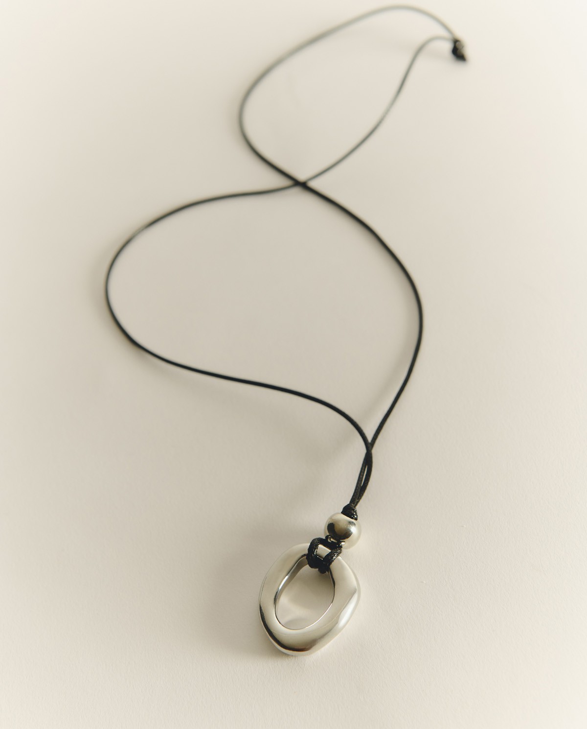 Collar llarg amb penjoll metàl·lic platejat i cordó negre