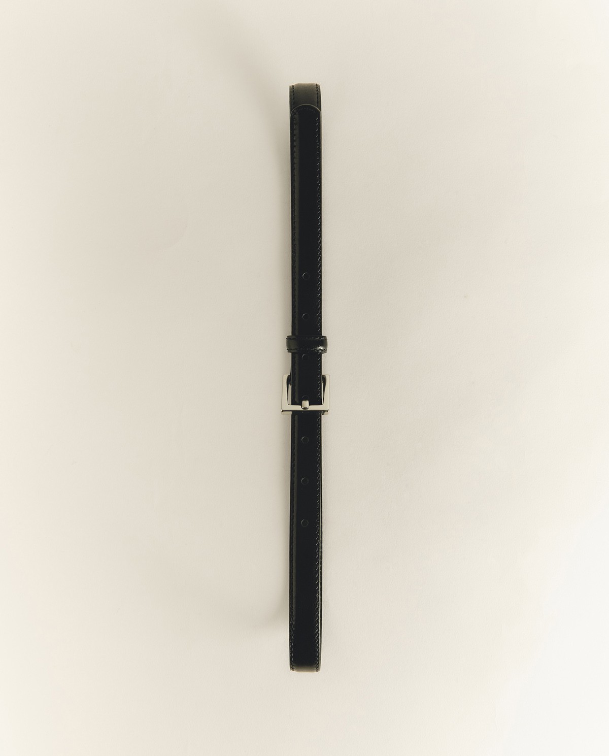 Cinturón fino con hebilla plateada en color negro, vista frontal con detalle del tejido